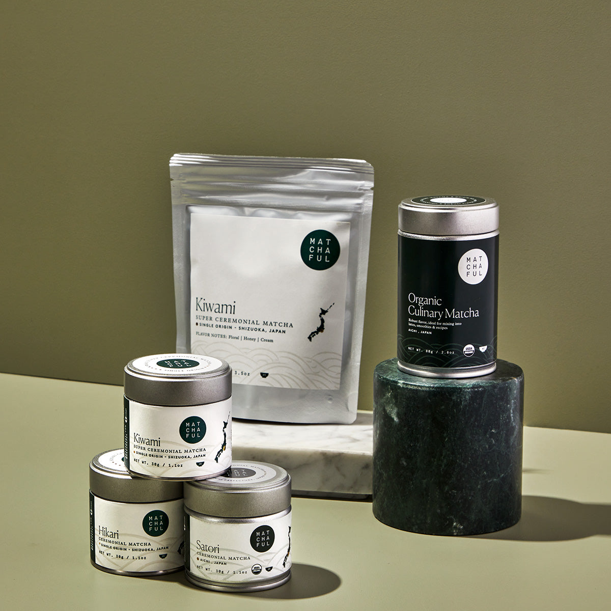 A trio of ceremonial matcha tins stacked in a pyramid with a ceremonial matcha bag and culinary matcha tin in the background