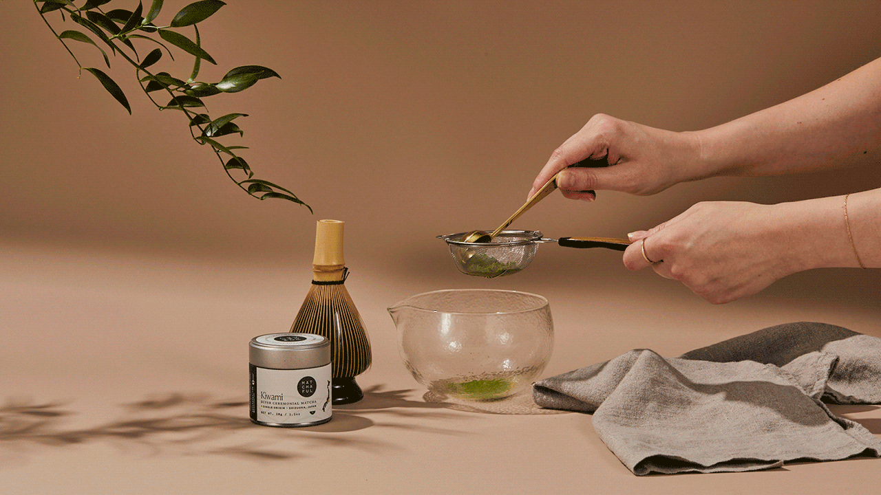 Gif of hands sifting matcha into a glass whisking bowl