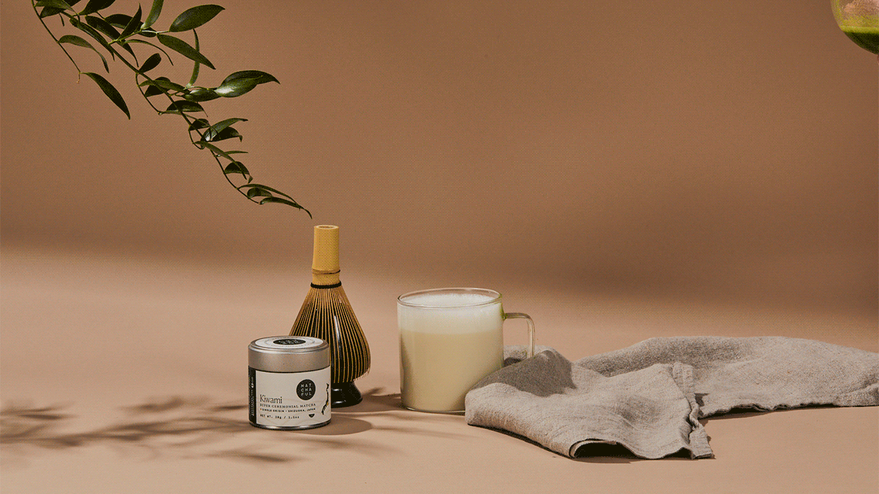 Gif of hands pouring matcha from a glass whisking bowl into a glass cup of foamy steamed milk