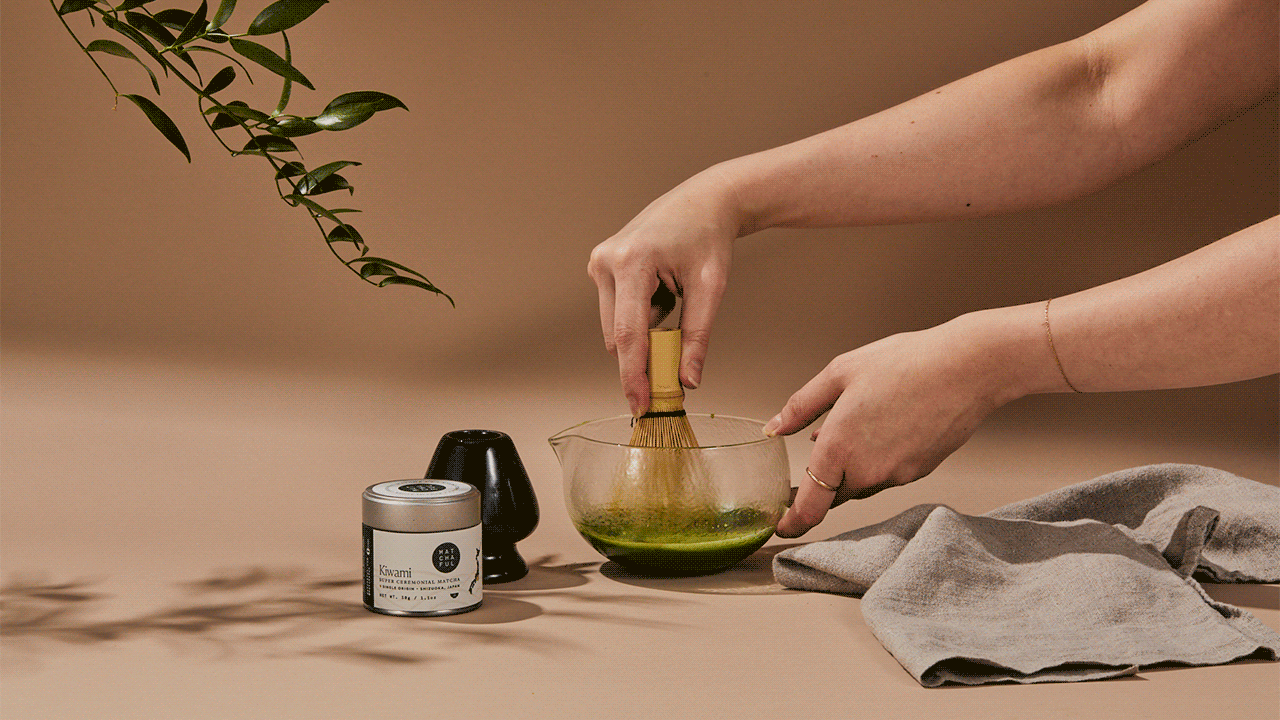 Gif of hands whisking matcha in a glass whisking bowl with a bamboo whisk