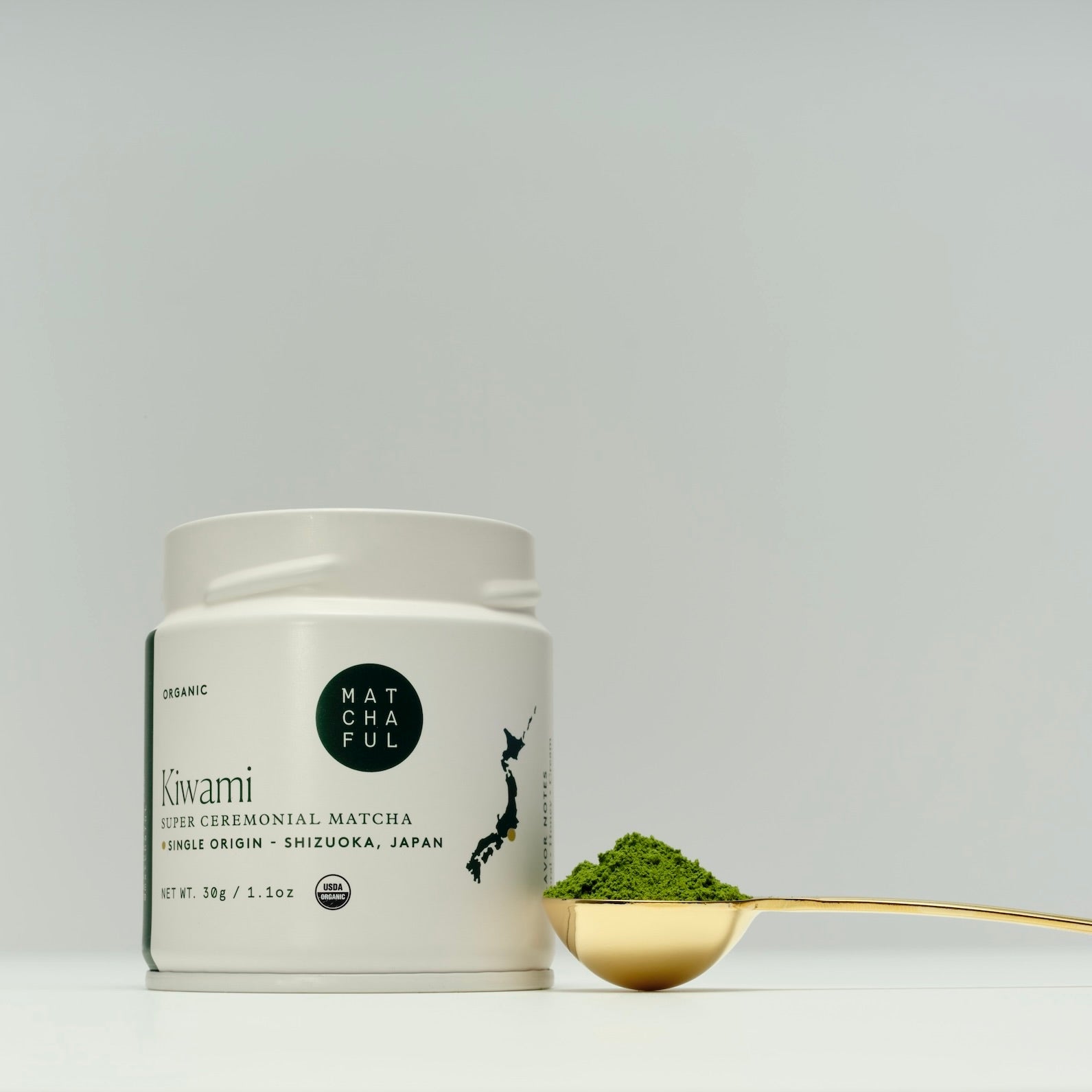 Matcha powder container with a spoonful of green powder on a light gray background