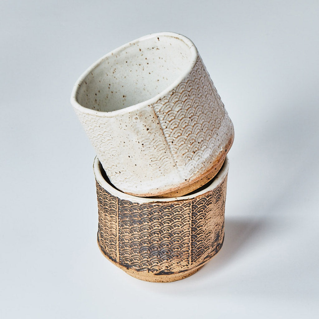 Stack of two ceramic matcha tea bowls with a Seigaiha pattern, one white glazed and the other natural clay
